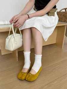Vue détaillée de chaussures plates fendues en daim jaune avec nœud et chaussettes.