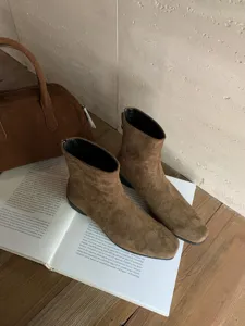 Gros plan de bottines marron en daim à talons carrés et bout carré sur livre d'art