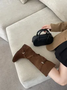 Vista detallada de botas altas de ante marrón con elegantes hebillas y cuña oculta.