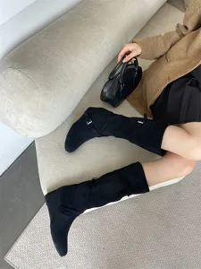 Detalle de botas altas de ante negro con correas laterales y textura de material suave.