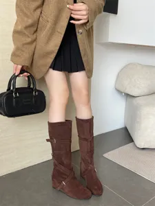 Detalle de botas altas de ante marrón con tirantes de hebilla y diseño de cuña.