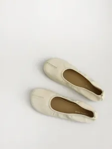 Close-up detail of beige split-toe soft leather flat shoes, minimalist design, comfortable.