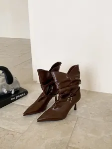 Vista detallada de botas marrones de tacón alto en punta con hebilla elegante y gran estilo.