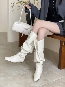Close-up detail shot of stylish white slouchy knee-high boots with square toe and chic buckles.