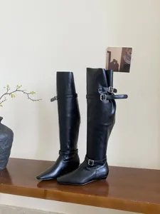 Women's chic black long boots with square toe, flat low heel, and stylish double buckle straps.