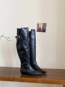 Black over-the-knee boots with low heels, flat soles, and metal buckle straps for French style.