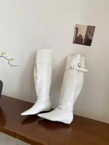 Stylish women's white long boots with pointed toe and low heel, perfect detail view.