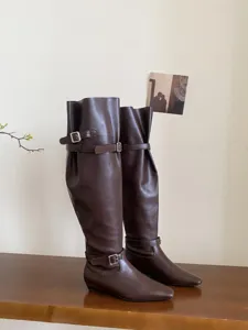 Brown slouchy knee high boots with metal buckles, low flat heel and chic square toe design.