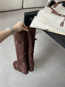 Vista detallada de botas altas de ante marrón con elegantes correas con hebilla.