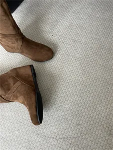 Vista detallada de botas de cuña de ante marrón en alfombra texturizada, gran estilo.