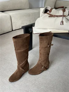 Vista detallada de botas altas de ante marrón con correas cruzadas y tacón de cuña.