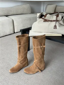 Detalle de botas de ante marrón con cuña, altura hasta la rodilla con correa y hebilla.