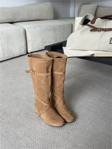 Detalle de botas altas de ante marrón con correas de hebilla y elegante diseño cruzado.