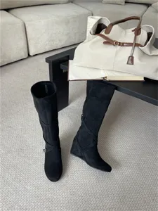 Detalle de botas altas de cuña en ante negro con tiras cruzadas y hebilla lateral.