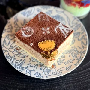 Torta tiramisù quadrata con motivo monogramma di cacao e topper in acrilico dorato.