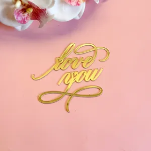 Gros plan détail de la décoration de gâteau love you en acrylique doré sur fond rose.
