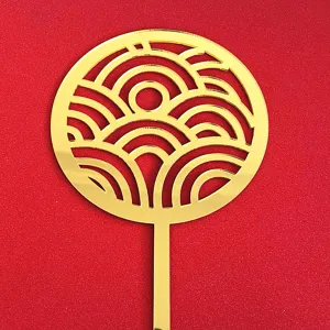Gold acrylic cake topper detail close up, traditional wave pattern Chinese style decoration.