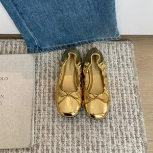 Detailopname van gouden ballerina's, zacht materiaal, elegante strik en comfortabele platte zool.