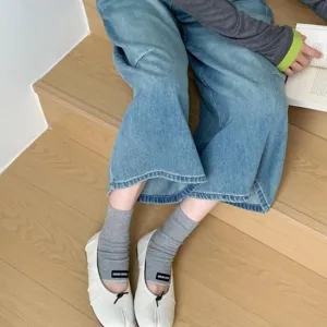 Close-up of split-toe ballet flats paired with gray socks and denim pants on wooden stairs.