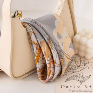 Luxurious mulberry silk scarf draped elegantly on a cream handbag with artistic nautical print.