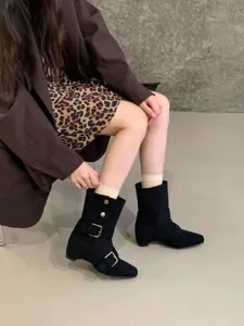 Détail de bottes mi-mollet en suédine noire avec boucle métallique et talon bloc.