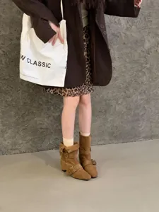 Gros plan sur les bottes mi-mollet en daim marron, talon carré rétro avec boucles élégantes.