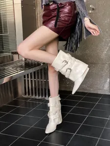 Vue détaillée de bottes souples en cuir blanc à bout pointu, brides bouclées et clous.