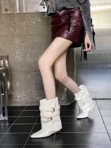 Gros plan sur des bottines blanches à talons compensés pointus avec brides à boucles.