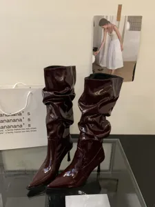 Botas altas de charol burdeos con tacón de aguja y diseño plisado, detalle de moda.