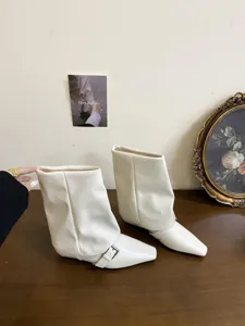 Primo piano dettagliato di eleganti stivaletti color crema con punta quadrata e fibbia.