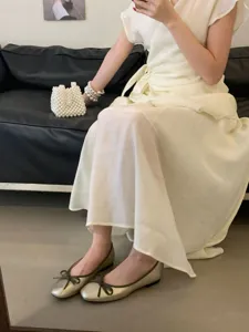 Detailed shot of French square toe bow flat ballet shoes worn with elegant white dress.