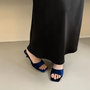 Detail view of elegant blue velvet square toe kitten heel mule sandals worn with a black skirt.