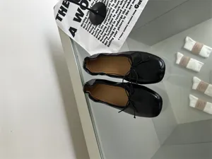 Detail view of black soft leather flat ballet shoes, featuring delicate bow tie and shallow cut.