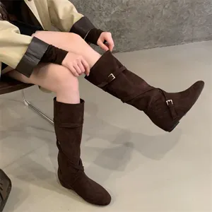 Detail of retro brown suede slouch boots with crossover buckle straps and hidden wedge.