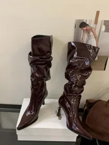 Vista detallada de botas plisadas de charol burdeos con tacón alto y puntera en punta.