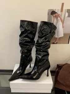Botas altas de charol negro con punta y tacón de aguja, vista detallada de textura.