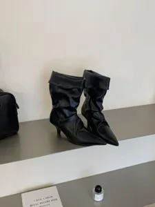 Botas de media caña negras con punta fina, tacón de aguja y elegante detalle fruncido.