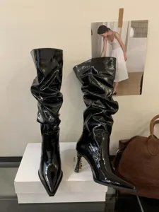 Vista detallada de botas slouchy de charol negro con punta afilada y tacón de aguja.