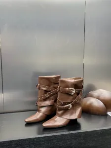 Detail de bottes marron a talon compense et bout pointu avec brides, boucles metal et clous.
