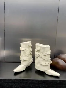Bottes mi-mollet blanches à bout pointu avec multiples brides bouclées et clous, style chic.