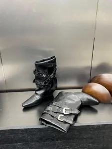 Bottes mi-hautes en cuir noir avec brides à boucles et détails de clous élégants.