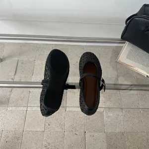 Dettaglio di scarpe Mary Jane intrecciate nere, design cavo traspirante con cinturino e fibbia.