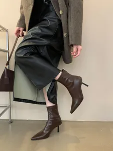 Primer plano de elegantes botines de punta fina con tacón alto en piel de charol marrón.