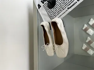 White patent leather flat ballet shoes detail shot, minimalist design with cute bow.