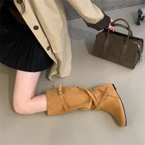 Detailed shot of retro suede slouchy long boots with cross buckle straps and wedge heel.