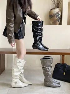 Detalle de botas altas fruncidas para mujer con puntera cuadrada y hebillas de metal chic.