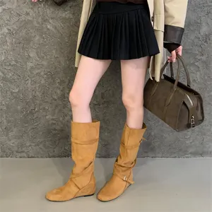 Detailed view of retro suede slouchy boots with cross strap buckles and hidden wedge heels.