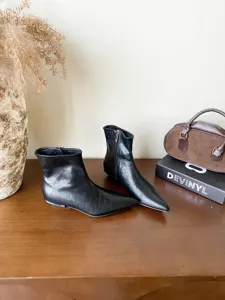 Vue détaillée de bottines noires élégantes à bout pointu et talon plat sur une table.