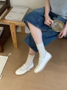 Vue détaillée de chaussures Mary Jane plates blanches avec nœud et chaussettes sur sol en bois.