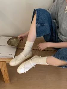 Gros plan détaillé de chaussures Mary Jane plates blanches avec lanière à nœud et chaussettes.
